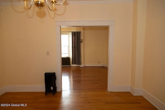 unfurnished room featuring ornamental molding, a chandelier, wood-type flooring, and radiator