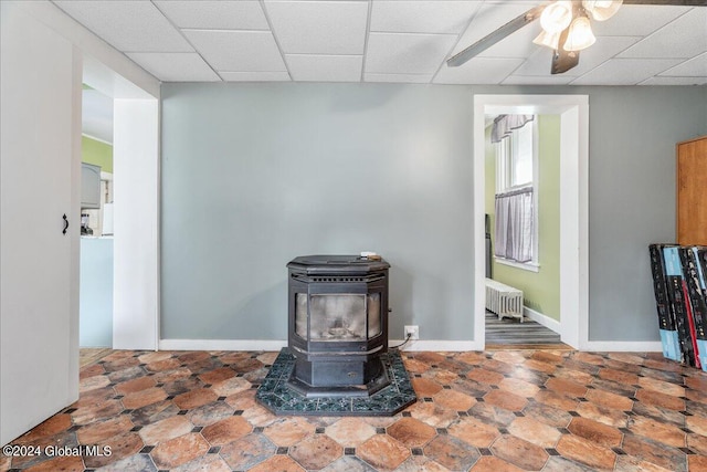 interior details with a paneled ceiling, ceiling fan, a wood stove, and radiator heating unit