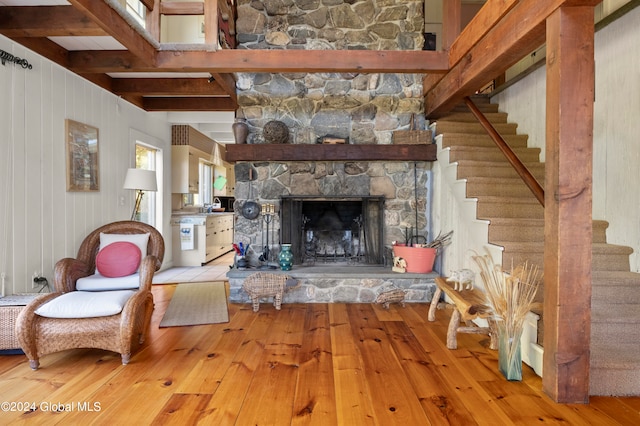 living room featuring a stone fireplace, beamed ceiling, light hardwood / wood-style flooring, and wooden walls