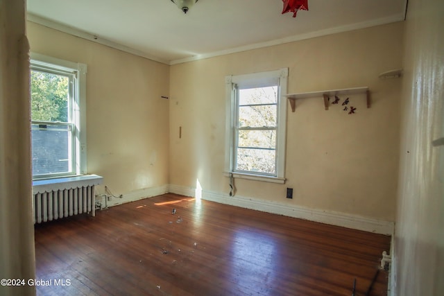 spare room featuring radiator, a healthy amount of sunlight, ornamental molding, and dark hardwood / wood-style floors