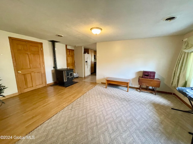 unfurnished room with a wood stove, light hardwood / wood-style floors, and a textured ceiling