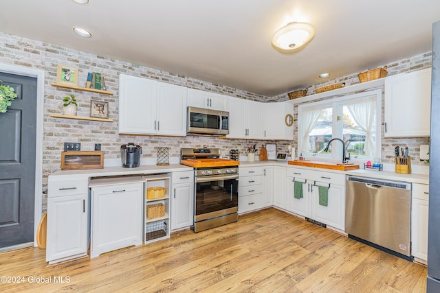 kitchen with appliances with stainless steel finishes, white cabinetry, sink, and light hardwood / wood-style floors