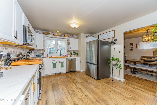 kitchen with white cabinets, hanging light fixtures, light hardwood / wood-style flooring, a notable chandelier, and stainless steel appliances