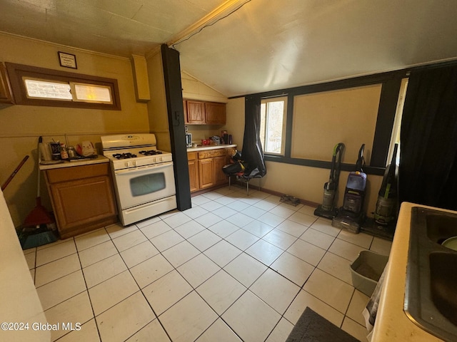 kitchen with light tile patterned flooring, gas range gas stove, sink, and vaulted ceiling