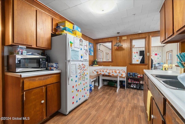 kitchen featuring light hardwood / wood-style flooring, wooden walls, sink, and white refrigerator