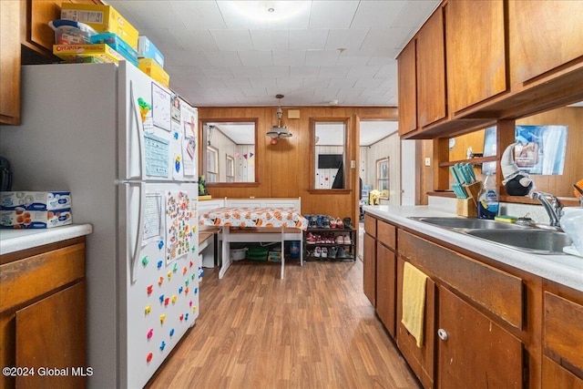 kitchen featuring white fridge, wood walls, hanging light fixtures, sink, and light hardwood / wood-style floors