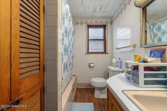 full bathroom with hardwood / wood-style flooring, shower / bath combo with shower curtain, vanity, toilet, and tile walls