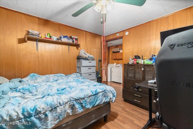 bedroom with light hardwood / wood-style flooring, wooden walls, ceiling fan, and washer and dryer