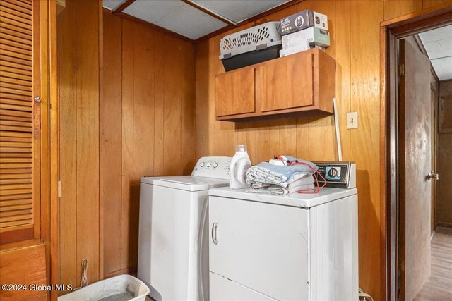 laundry area with wood walls, light hardwood / wood-style floors, washer and dryer, and cabinets