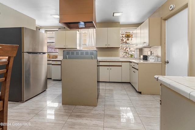 kitchen with light tile patterned flooring, stainless steel refrigerator, a kitchen island, and cream cabinets