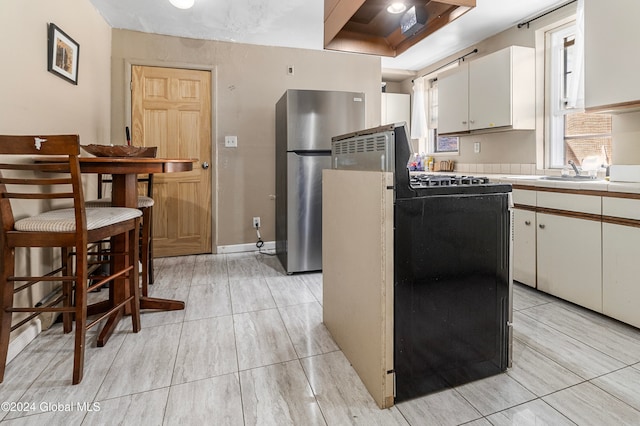 kitchen with black range oven, sink, stainless steel fridge, a raised ceiling, and white cabinetry