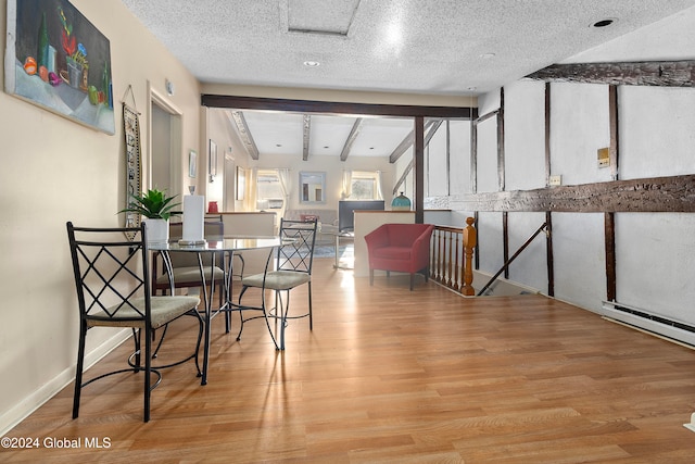 dining room featuring vaulted ceiling with beams, a textured ceiling, and light wood-type flooring