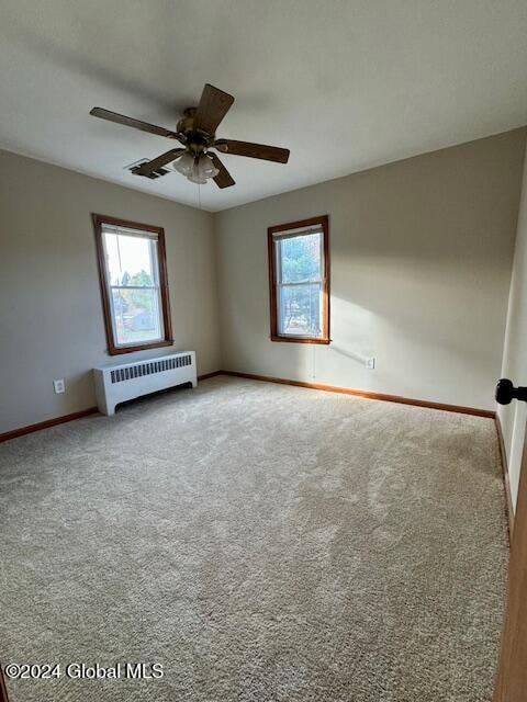 unfurnished room with radiator, ceiling fan, and carpet