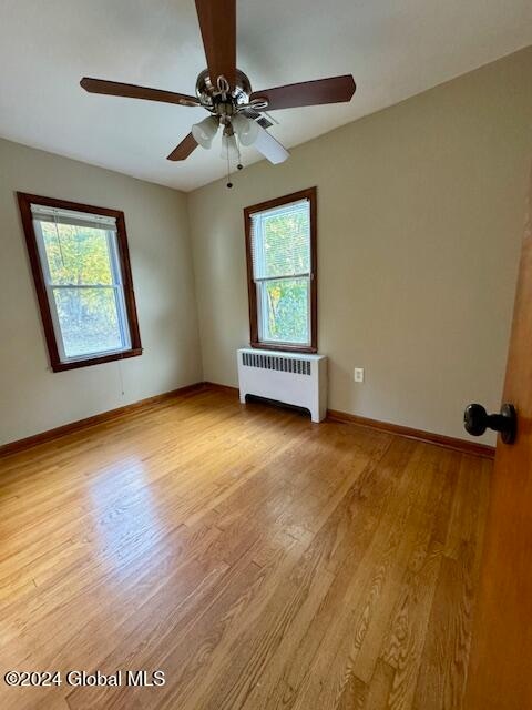 spare room featuring light hardwood / wood-style floors, ceiling fan, radiator, and a wealth of natural light