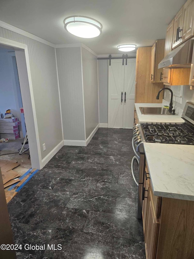 kitchen with light stone counters, ornamental molding, a barn door, stainless steel gas range, and sink