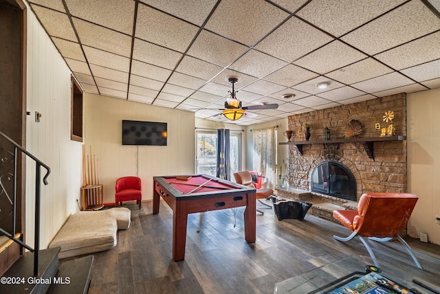 game room featuring hardwood / wood-style floors, a paneled ceiling, a stone fireplace, wooden walls, and ceiling fan