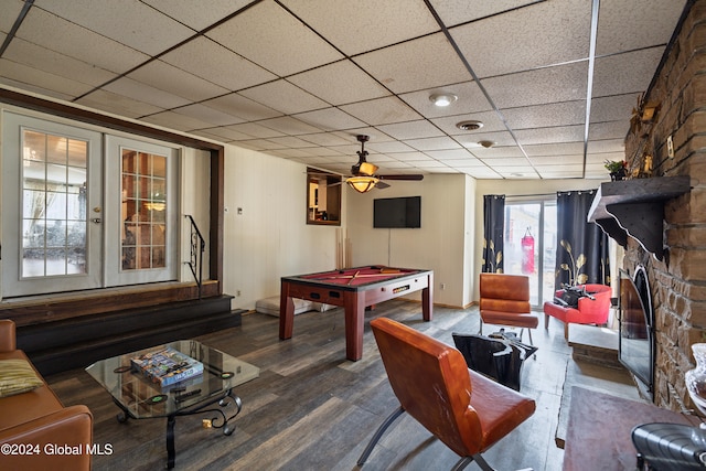 game room with french doors, a drop ceiling, ceiling fan, wood-type flooring, and a stone fireplace