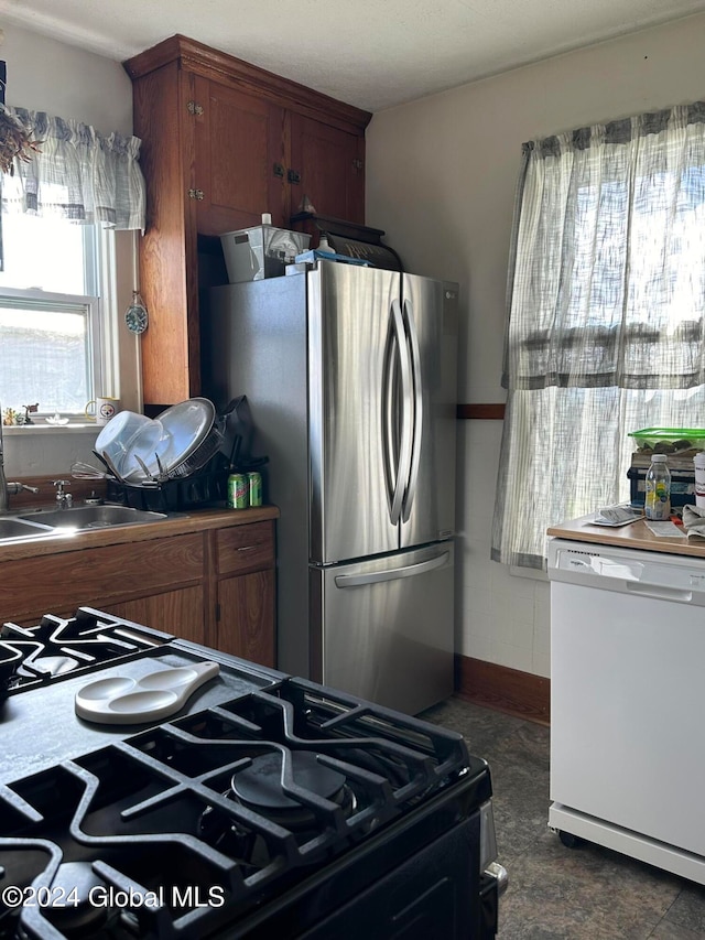 kitchen with stainless steel fridge, white dishwasher, sink, and black gas range oven