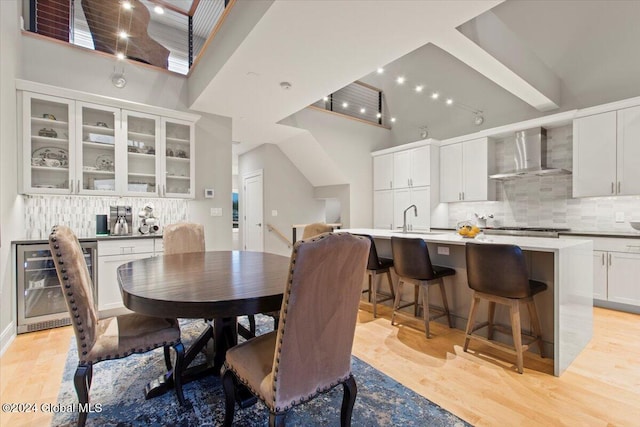 dining area featuring a towering ceiling, sink, wine cooler, and light hardwood / wood-style flooring