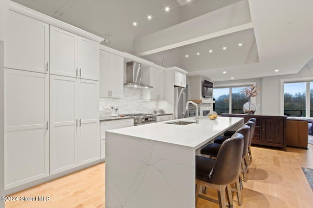 kitchen with white cabinets, sink, wall chimney exhaust hood, and an island with sink