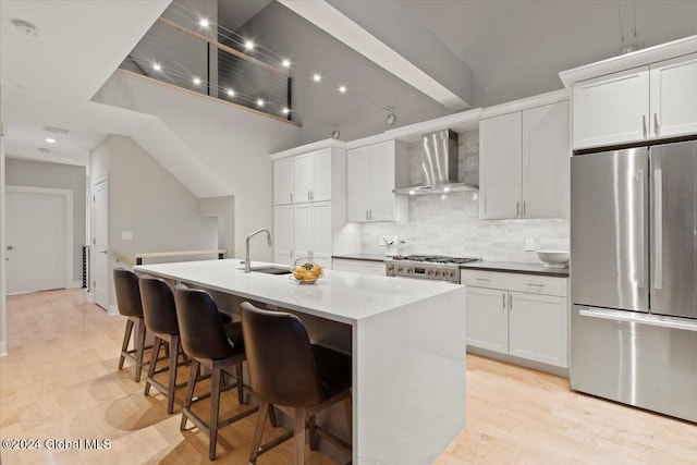 kitchen featuring stainless steel refrigerator, white cabinetry, sink, wall chimney range hood, and an island with sink