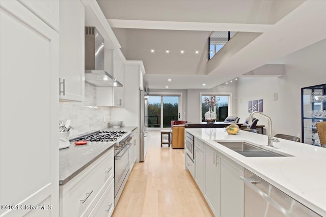 kitchen with white cabinetry, sink, stainless steel appliances, wall chimney range hood, and light stone counters