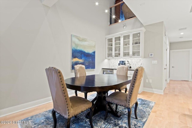 dining space featuring a towering ceiling and light hardwood / wood-style floors