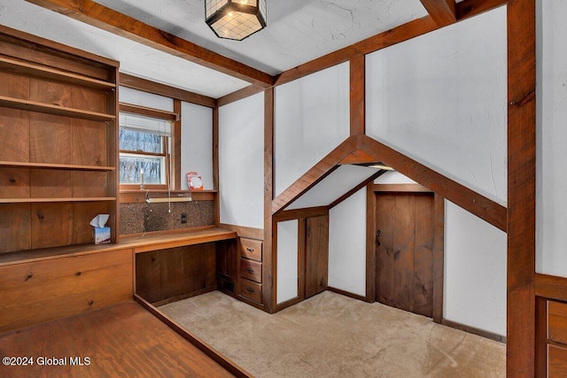 interior space with light colored carpet, beam ceiling, and built in desk