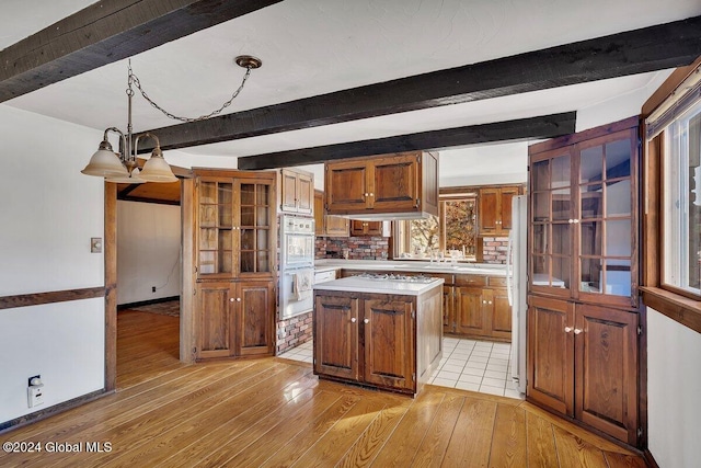 kitchen featuring tasteful backsplash, a kitchen island, light hardwood / wood-style floors, decorative light fixtures, and beam ceiling