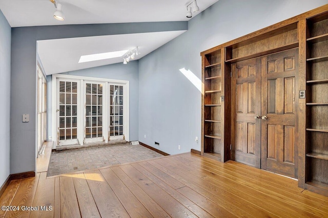 interior space with lofted ceiling with skylight, light hardwood / wood-style flooring, and rail lighting