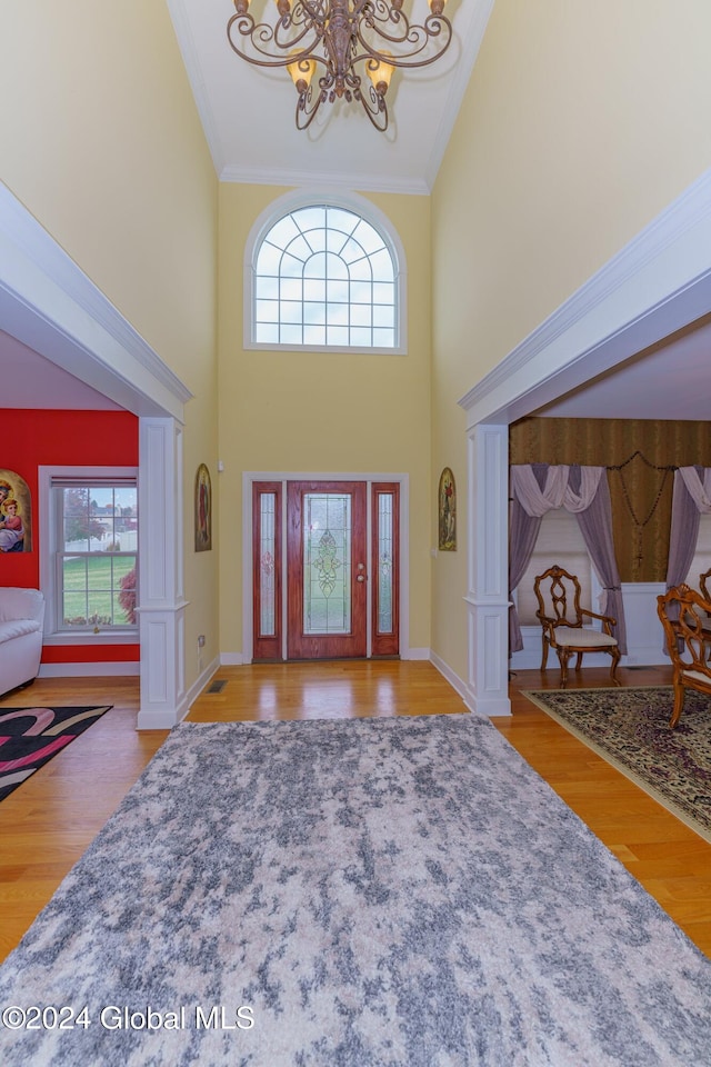 foyer entrance with crown molding, light hardwood / wood-style flooring, a towering ceiling, and decorative columns