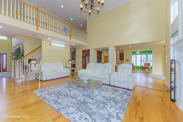 living room featuring a notable chandelier, a towering ceiling, light hardwood / wood-style flooring, and ornamental molding