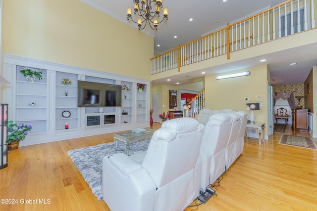 living room with built in features, an inviting chandelier, a high ceiling, and light wood-type flooring