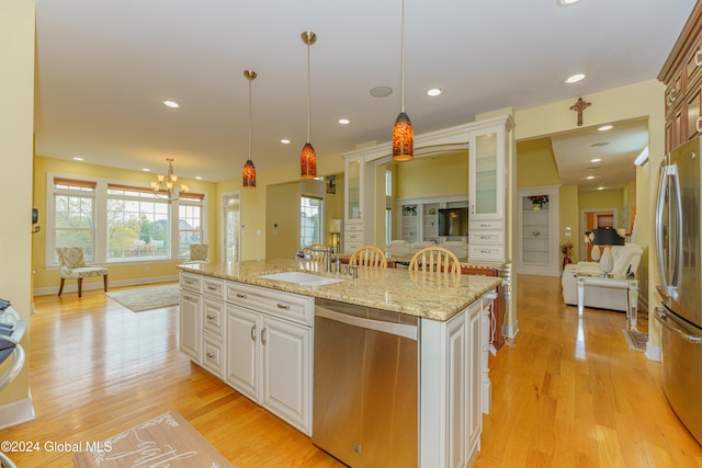 kitchen featuring a kitchen island with sink, hanging light fixtures, stainless steel appliances, sink, and white cabinetry