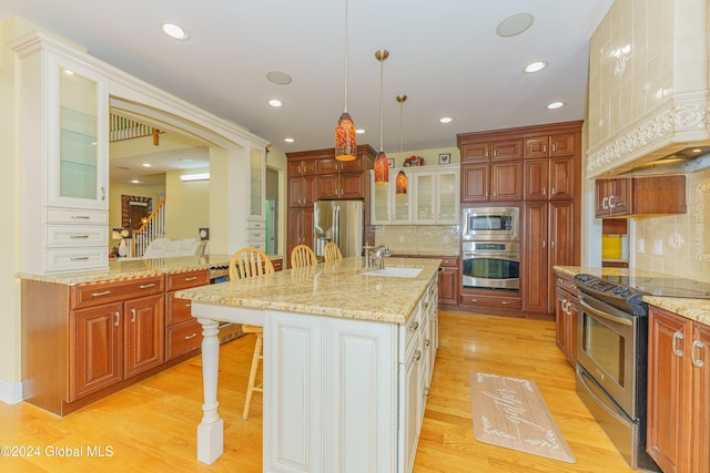 kitchen featuring tasteful backsplash, appliances with stainless steel finishes, a kitchen bar, pendant lighting, and a center island with sink