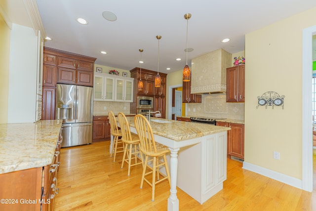 kitchen featuring a kitchen breakfast bar, stainless steel appliances, custom exhaust hood, light hardwood / wood-style flooring, and a kitchen island with sink