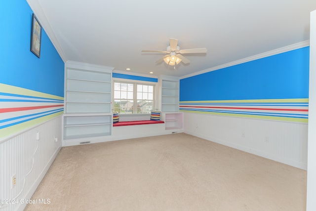 empty room featuring ornamental molding, light colored carpet, built in features, and ceiling fan