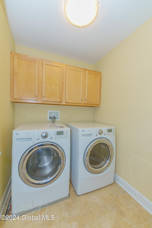 clothes washing area featuring washer and dryer, light tile patterned flooring, and cabinets