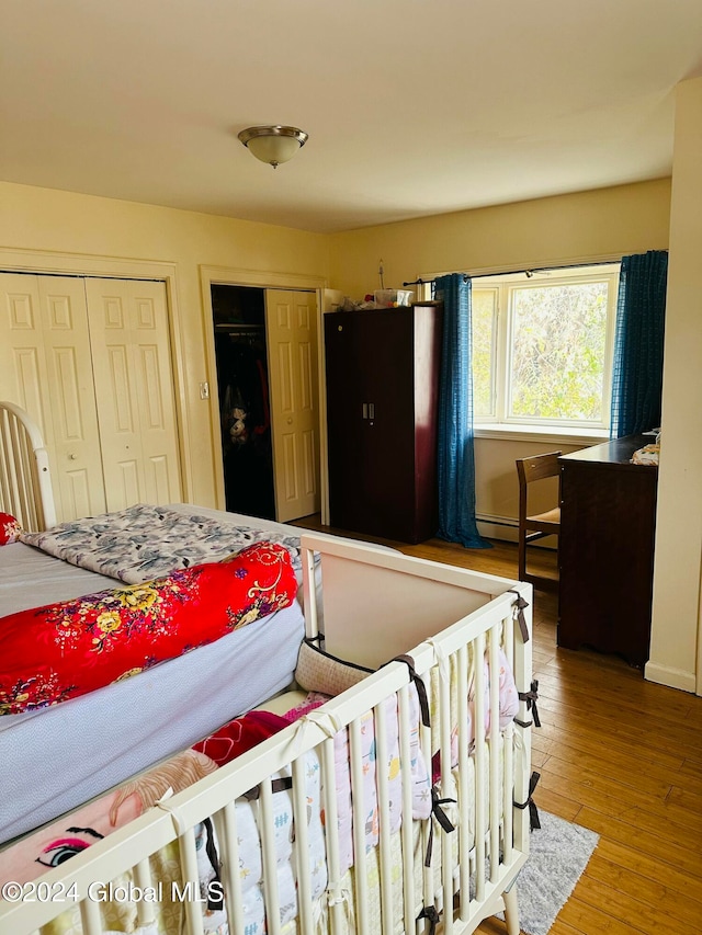 bedroom with a baseboard heating unit, hardwood / wood-style flooring, and two closets