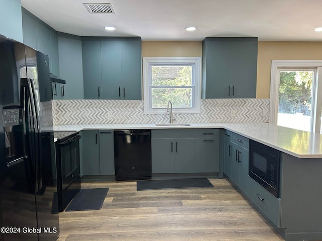 kitchen with decorative backsplash, kitchen peninsula, sink, black appliances, and light wood-type flooring