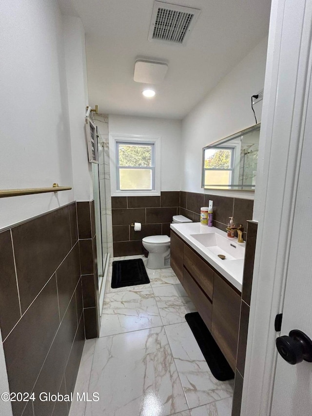 bathroom with tile walls, vanity, toilet, and an enclosed shower