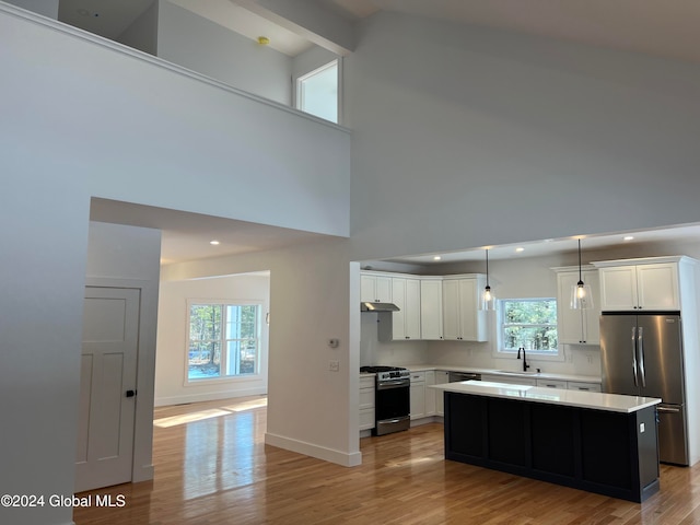 kitchen with hanging light fixtures, a kitchen island, appliances with stainless steel finishes, plenty of natural light, and a high ceiling