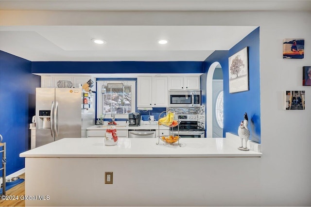 kitchen featuring backsplash, stainless steel appliances, white cabinetry, and hardwood / wood-style flooring