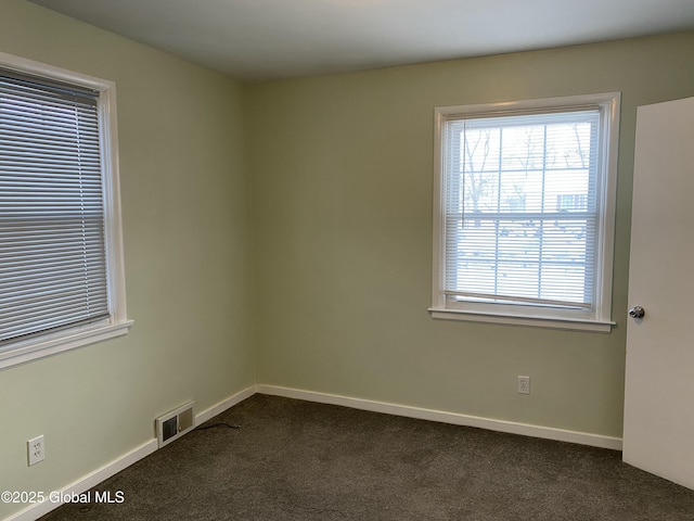 spare room with visible vents, dark carpet, and baseboards