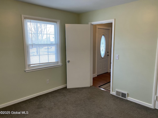 unfurnished room featuring baseboards, visible vents, and dark carpet