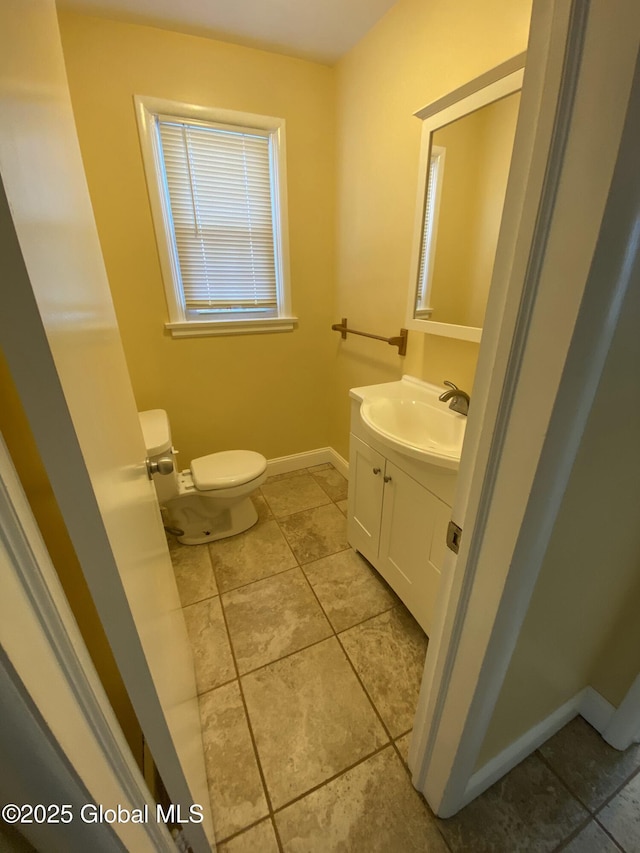 half bath with toilet, tile patterned flooring, vanity, and baseboards