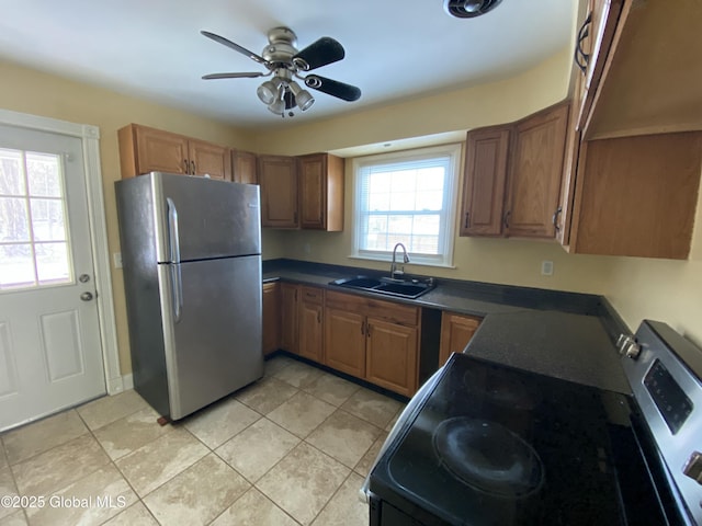 kitchen featuring ceiling fan, a sink, appliances with stainless steel finishes, brown cabinetry, and dark countertops