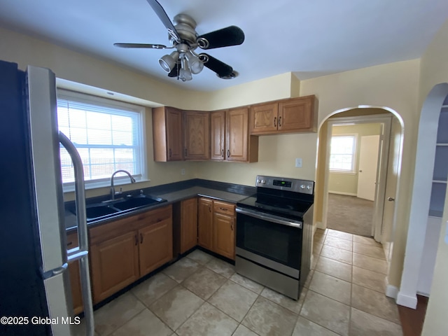 kitchen featuring arched walkways, stainless steel appliances, dark countertops, a ceiling fan, and a sink