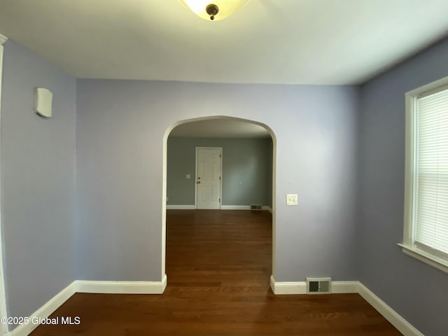 spare room featuring baseboards, visible vents, arched walkways, and wood finished floors