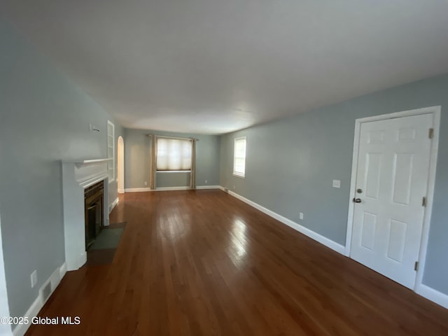 unfurnished living room featuring wood finished floors, a fireplace with flush hearth, visible vents, and baseboards